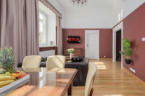 Ein modernes Wohnzimmer mit einem Glastisch, zwei Sesseln, einem Sofa, einem an der Wand montierten Fernseher und einer Topfpflanze.