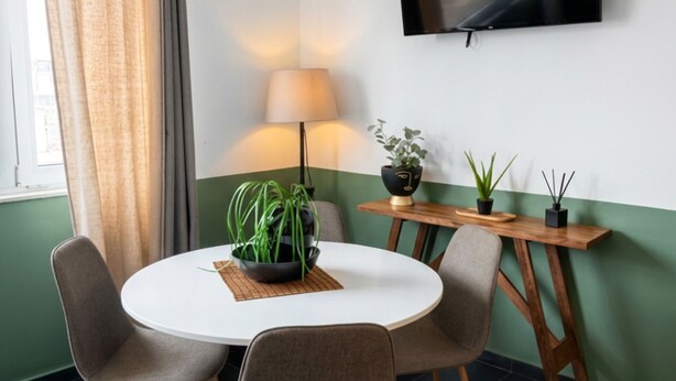 Uma sala de jantar moderna com uma mesa redonda, quatro cadeiras, uma TV na parede, um abajur e duas plantas em vasos.