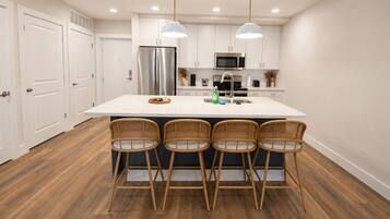 A modern kitchen with a central island, bar stools, stainless steel appliances, and white cabinetry.