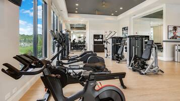 A modern gym with cardio equipment, weight machines, and a large window offering a view of the outdoors.