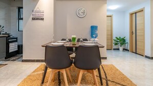 Zona pranzo con tavolo imbandito per quattro persone, orologio a parete e cartello con testo motivazionale.