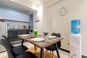 Una cocina moderna con armarios blancos, una mesa de comedor con platos, vasos y un dispensador de agua.