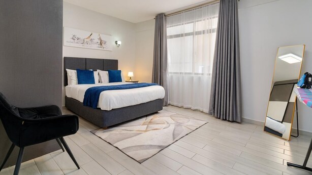 Una camera d'albergo con un letto, una sedia, una scrivania con uno specchio e una finestra con tende.