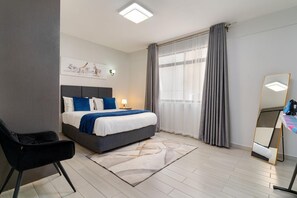 A hotel room with a bed, a chair, a desk with a mirror, and a window with curtains. - Diamond Homes View Palace Apartment (Nairobi)