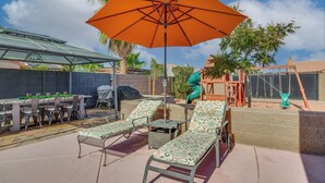 Een terras buiten met twee loungesteunen, een tafel en een parasol.