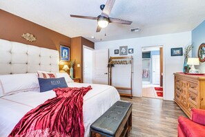 Ein Schlafzimmer mit einem großen Bett, einem Deckenventilator, einer Holzkommode und einer Tür zu einem anderen Raum.