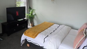 A bedroom with a bed, a TV on a stand, a plant, and a wall decoration.