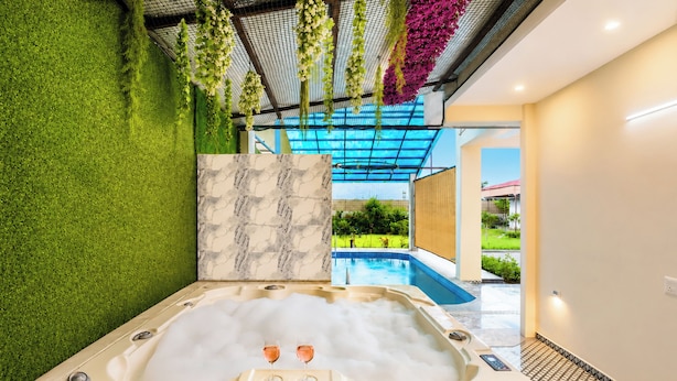A spa area with a hot tub, green artificial grass, a marble wall, and a view of a swimming pool. - Alaya Stays JSP Farm 4BHK Farmstay (Jaipur)