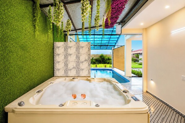 A spa area with a hot tub, green artificial grass, a marble wall, and a view of a swimming pool.