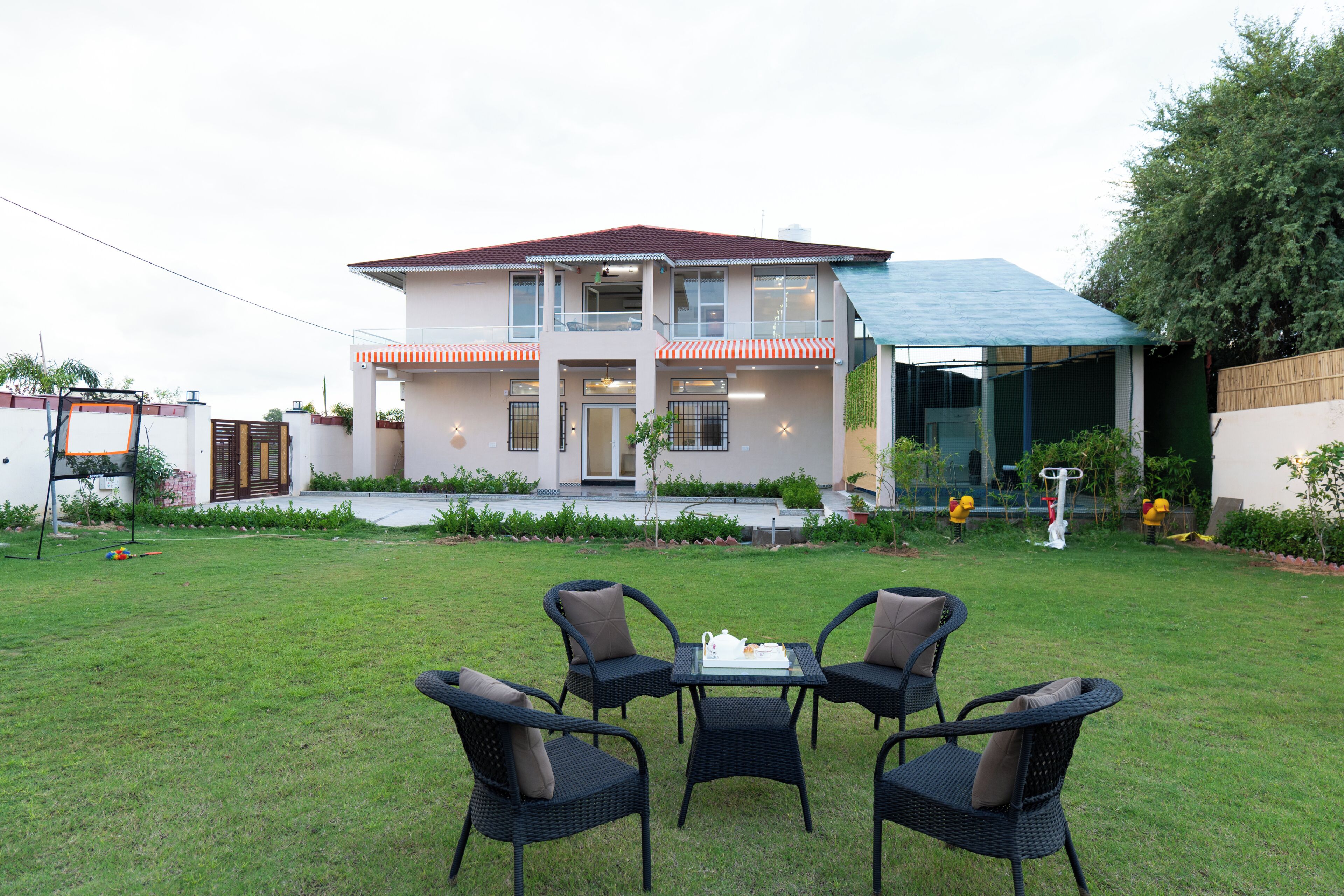 A two-story house with a balcony, a covered outdoor area, and a lawn with outdoor furniture.