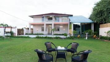 A two-story house with a balcony, a covered outdoor area, and a lawn with outdoor furniture.