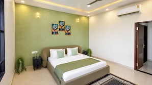 A modern bedroom with a bed, nightstands, a ceiling fan, wall-mounted air conditioning, and decorative wall art. - Alaya Stays JSP Farm 4BHK Farmstay (Jaipur)