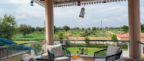 A covered outdoor seating area with chairs and a table, overlooking a green landscape with buildings in the distance.
