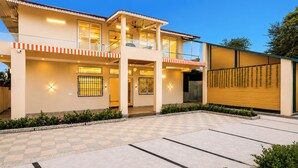 A two-story building with a balcony, a covered entrance, and a checkered driveway. - Alaya Stays JSP Farm 4BHK Farmstay (Jaipur)