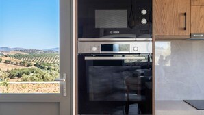 A kitchen with a Bosch microwave and oven, a window with a view of hills, and wooden cabinets. - Villa Vision | Brand New, Private Pool & Seaviews (Chania)