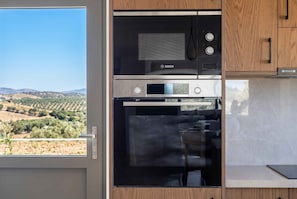 A kitchen with a Bosch microwave and oven, a window with a view of hills, and wooden cabinets. - Villa Vision | Brand New, Private Pool & Seaviews (Chania)