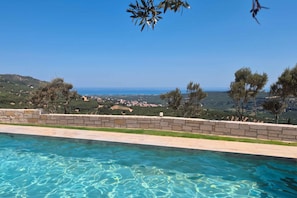 A swimming pool with clear blue water, surrounded by a stone wall and overlooking a coastal landscape with trees and a view of the sea. - Villa Vision | Brand New, Private Pool & Seaviews (Chania)