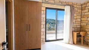 A room with a wooden wardrobe, a balcony with a stone wall, and a view of a hilly landscape. - Villa Vision | Brand New, Private Pool & Seaviews (Chania)