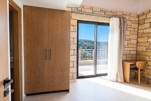 A room with a wooden wardrobe, a balcony with a stone wall, and a view of a hilly landscape. - Villa Vision | Brand New, Private Pool & Seaviews (Chania)
