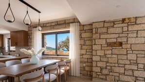 A modern kitchen with stone walls, a dining area with a table and chairs, and a view of the outdoors. - Villa Vision | Brand New, Private Pool & Seaviews (Chania)