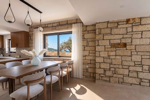 A modern kitchen with stone walls, a dining area with a table and chairs, and a view of the outdoors. - Villa Vision | Brand New, Private Pool & Seaviews (Chania)