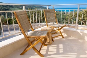 Two wooden lounge chairs with woven seats and backs, positioned on a balcony with a white railing, overlooking a coastal landscape. - Villa Vision | Brand New, Private Pool & Seaviews (Chania)