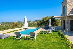 A pool area with lounge chairs and umbrellas, surrounded by a well-maintained lawn and a stone building. - Villa Vision | Brand New, Private Pool & Seaviews (Chania)