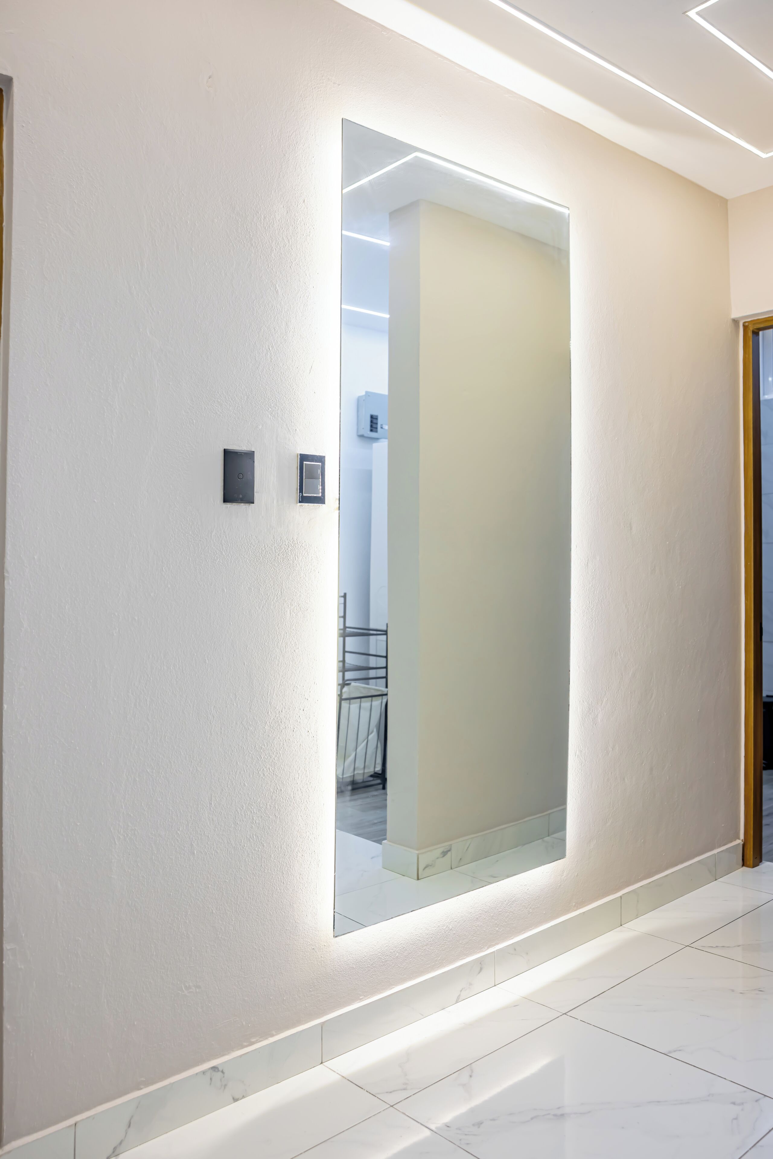 A hallway with a large mirror, a door, and a light fixture.