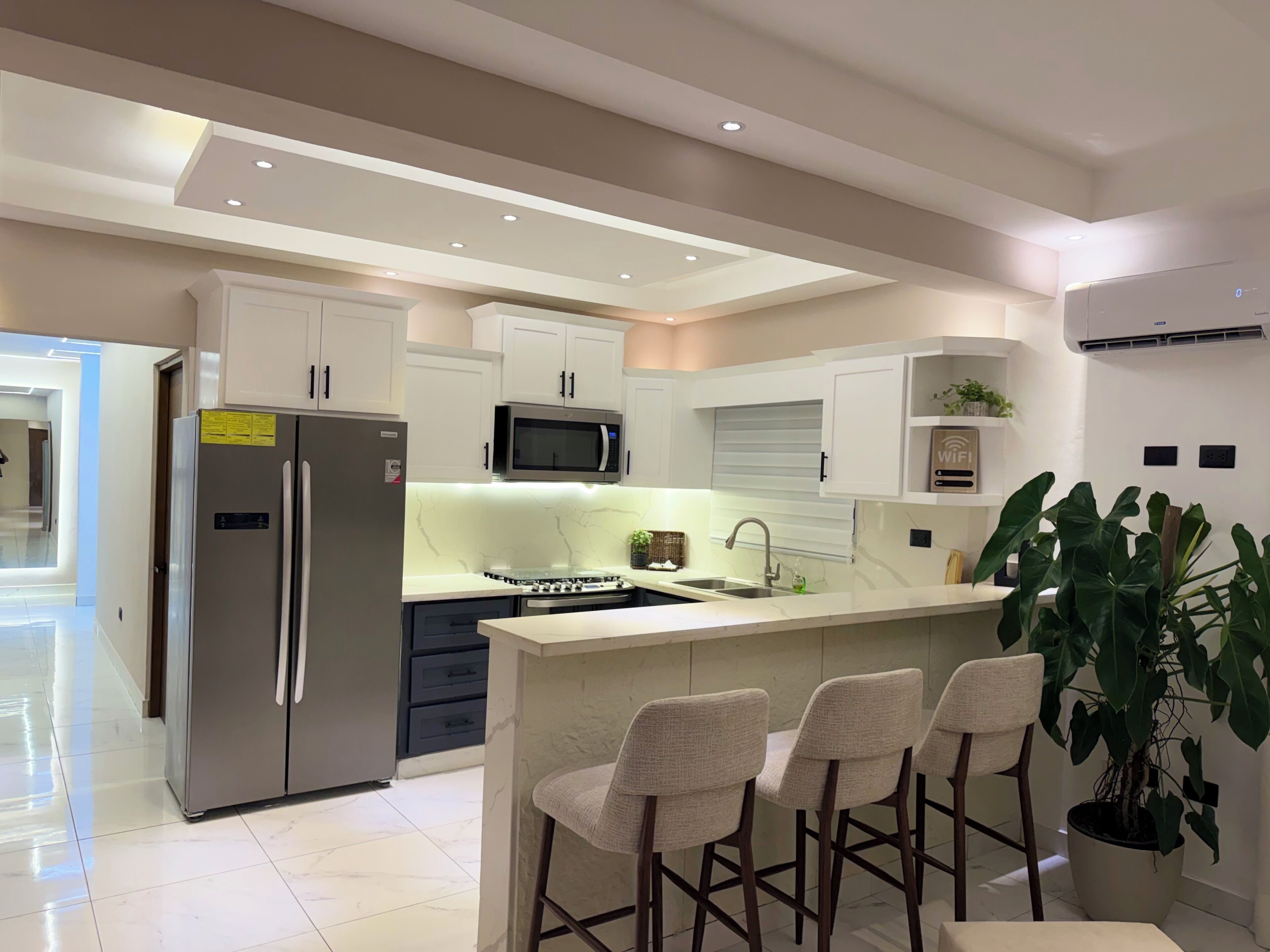 A modern kitchen with a central island, bar stools, a refrigerator, microwave, and a sink.