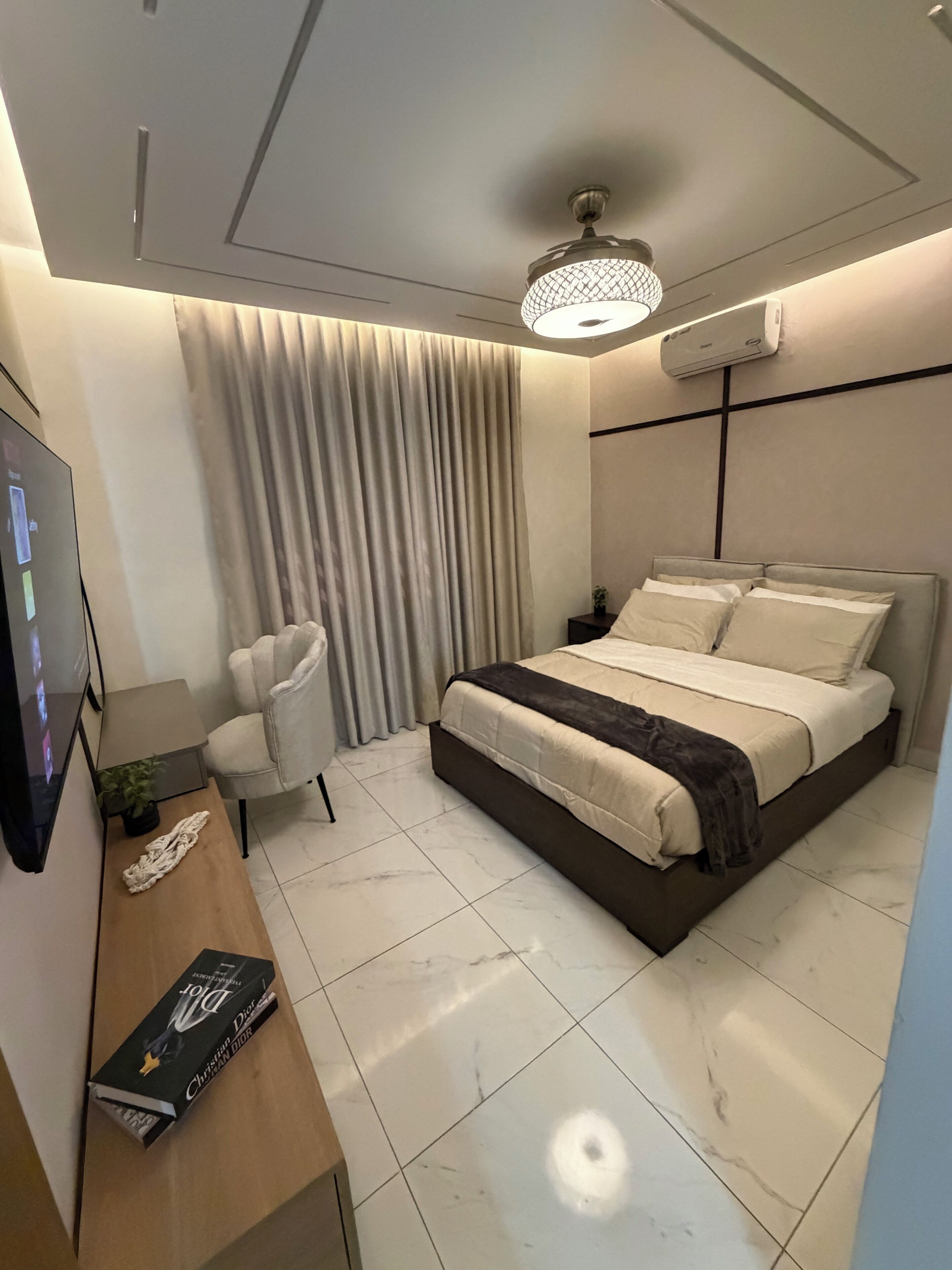 A modern bedroom with a bed, a desk, a chair, and a television.