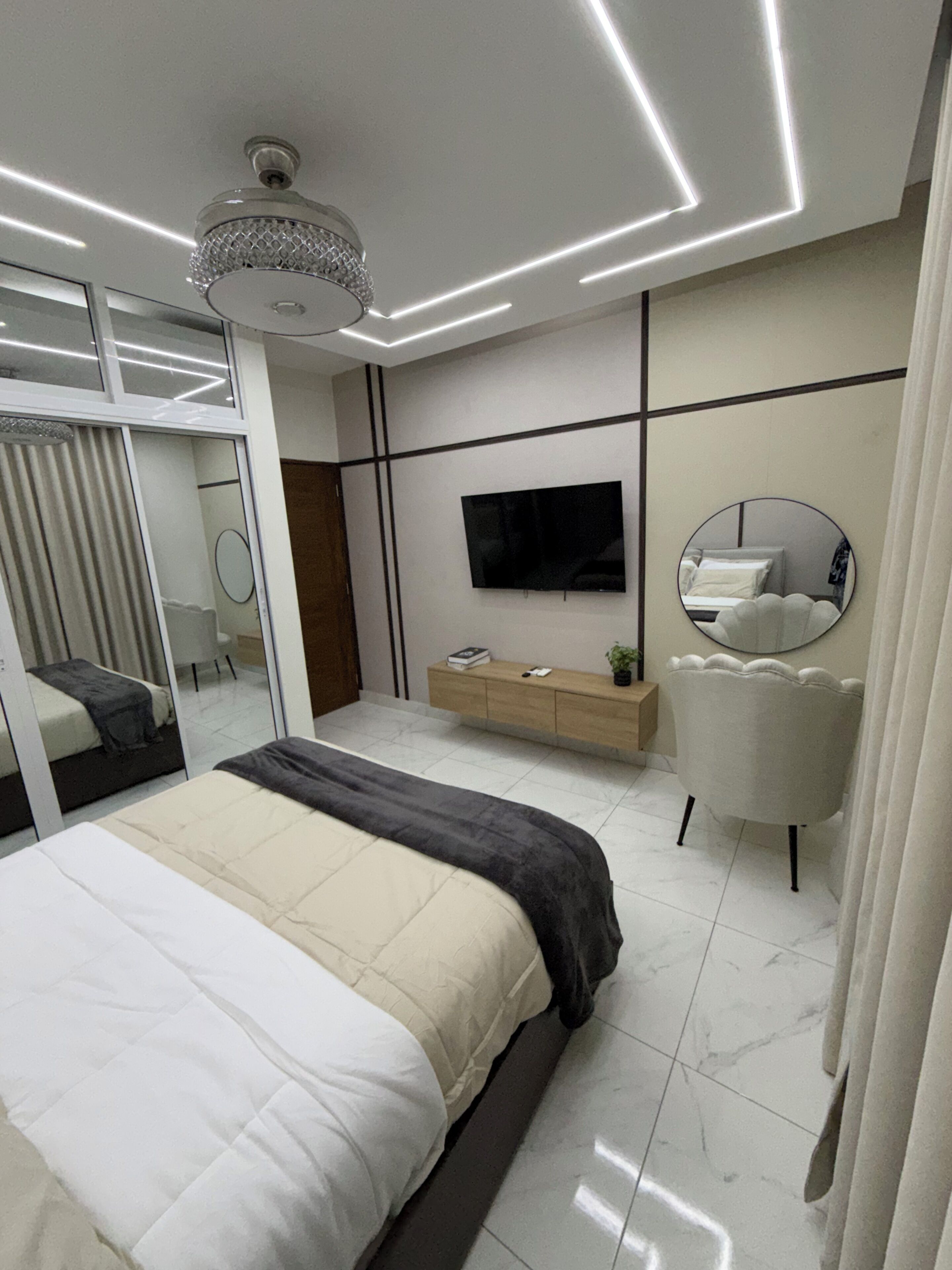 Ein modernes Schlafzimmer mit einem Bett, einem Fernseher, einem Spiegel und einer Deckenleuchte.