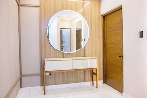 Een badkamer met een houten wastafelmeubel, een ronde spiegel en een witte deur.