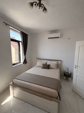 Ein Schlafzimmer mit einem Bett, einem Fenster mit Vorhängen, einer Klimaanlage und einer Tür.