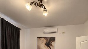 A neatly made bed with a headboard, a bedside table, a wall-mounted air conditioner, and a door to the right. - Luxury Stay in the City Center (Bucharest)