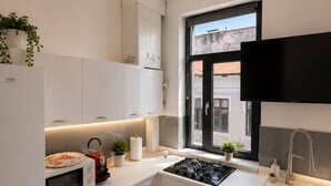 A modern kitchen with white cabinetry, a built-in stove, a microwave, and a window with a view of the outside. - Luxury Stay in the City Center (Bucharest)