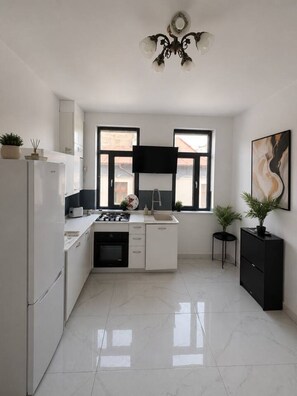 A modern kitchen with white cabinetry, a black countertop, a built-in oven, a sink, and a television mounted above the windows. - Luxury Stay in the City Center (Bucharest)