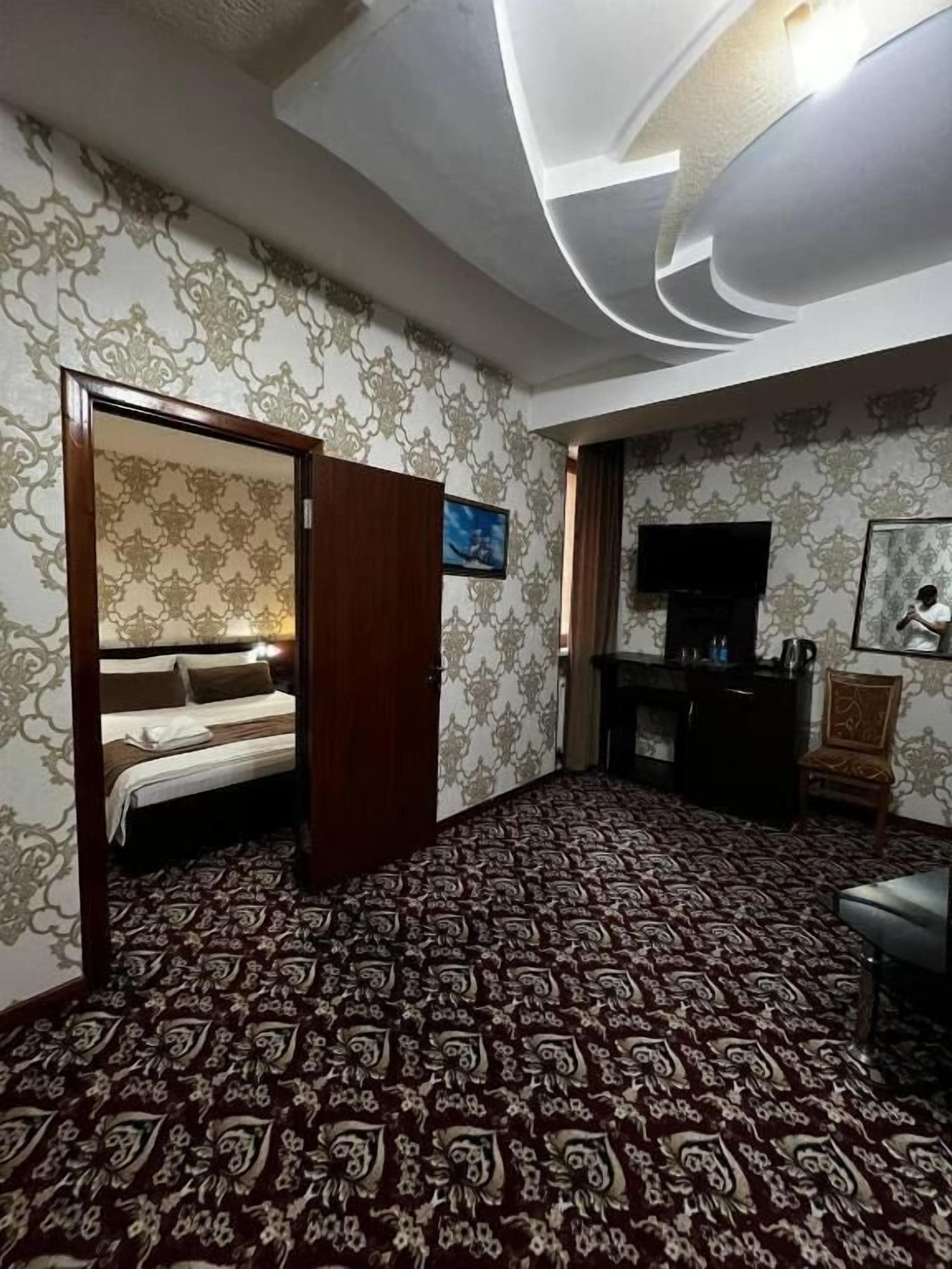 A hotel room with a patterned carpet, a bed, a television, and a wall-mounted TV.