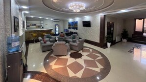 Um saguão de hotel com balcão de recepção, área de estar e um padrão circular decorativo no chão.