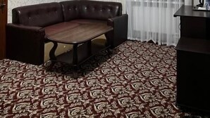 Quarto com sofá, mesa, carpete estampado, luminária no teto e janela com cortinas.