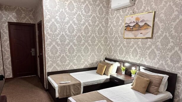 Quarto de hotel com duas camas, uma mesa de cabeceira com abajur, ar-condicionado na parede e um quadro emoldurado.
