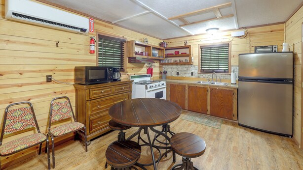 A compact kitchen with wooden cabinetry, a dining table, a refrigerator, and a microwave.