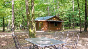 A rustic wooden cabin with a metal table and chairs in a forest setting.