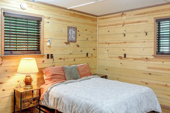 A wooden-paneled room with a bed, a nightstand, a lamp, and a wall-mounted thermostat.