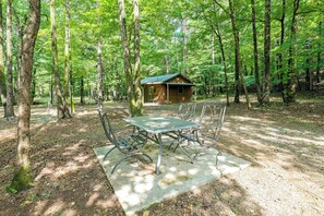 A rustic wooden cabin surrounded by a forest, with a picnic table and chairs in the foreground.