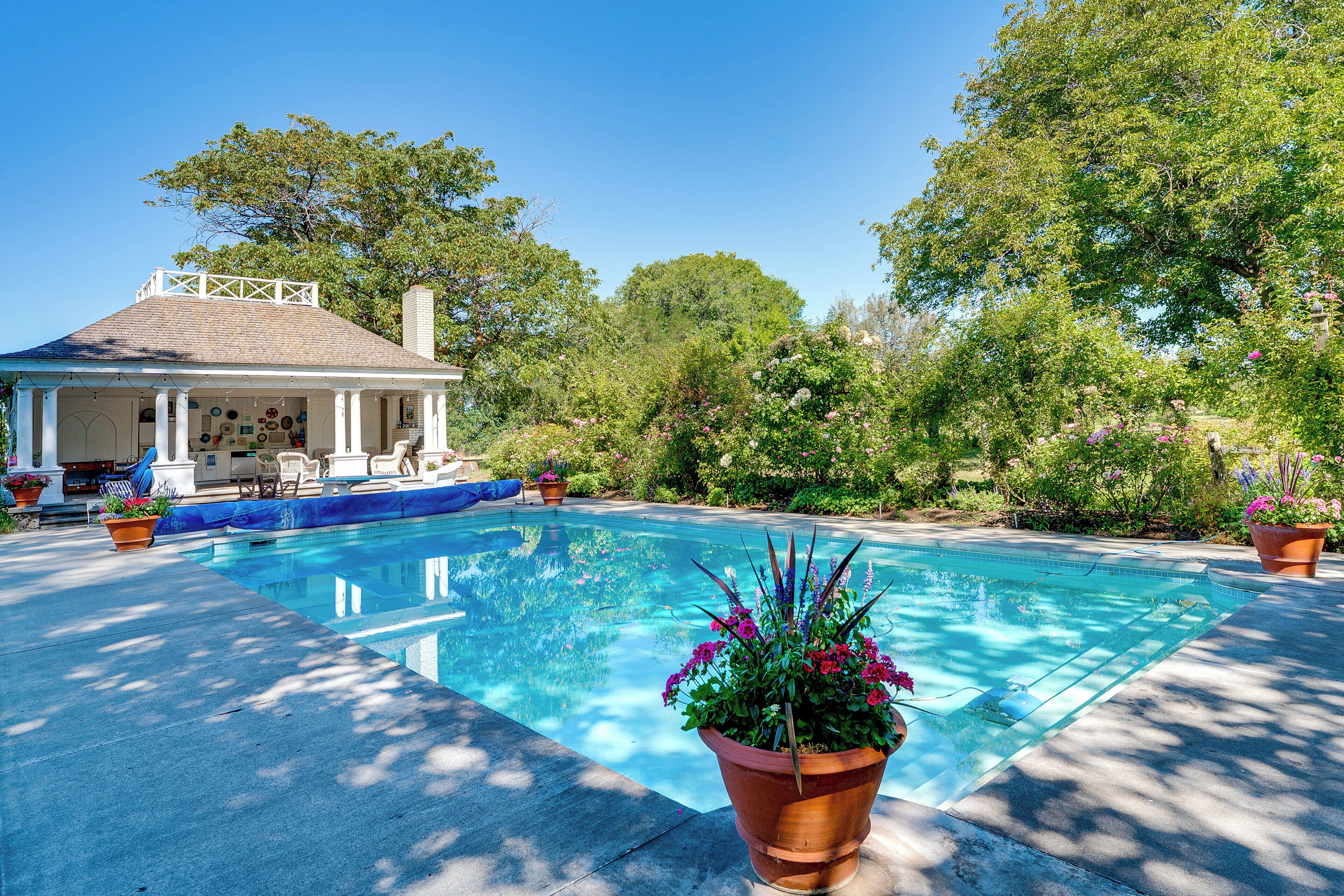 A swimming pool with a covered patio area, surrounded by lush greenery and trees.