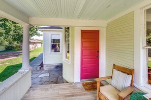 Eine Veranda mit roter Tür, einer Holzbank mit Kissen und einem kleinen Tisch.