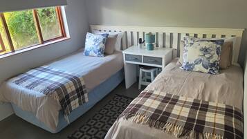 A bedroom with two single beds, a desk, and a window.