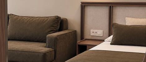 A hotel room with a bed, a sofa, a nightstand, and a mirror.