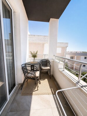 Ein Balkon mit Tisch, zwei Stühlen, einer Topfpflanze und Blick auf Gebäude.