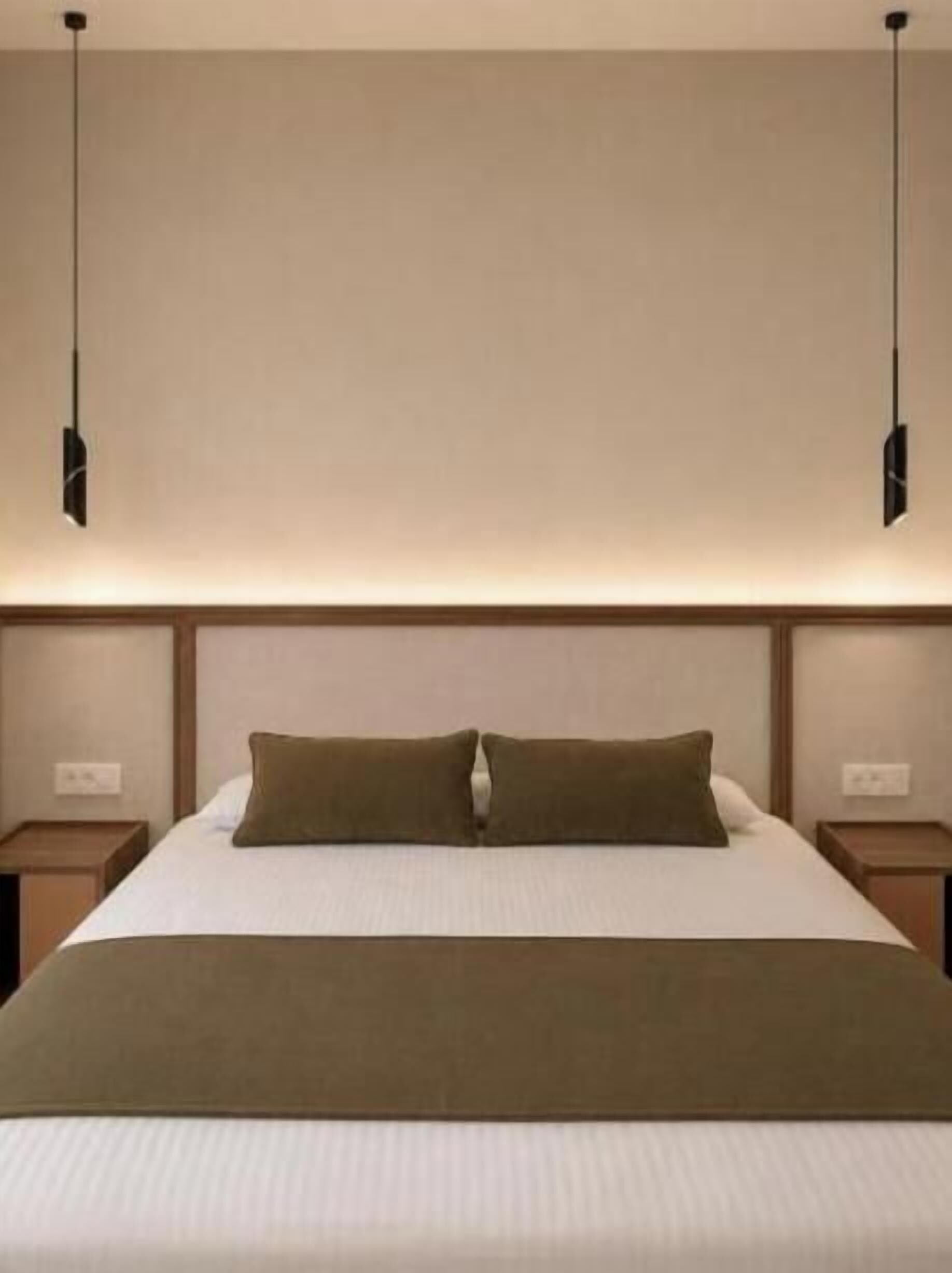 A hotel room with a large bed, two bedside tables, and a hanging light fixture.